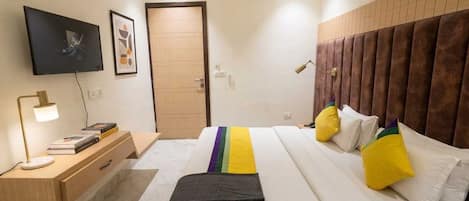 A modern hotel room with a bed, bedside table, lamp, and a TV on the wall.