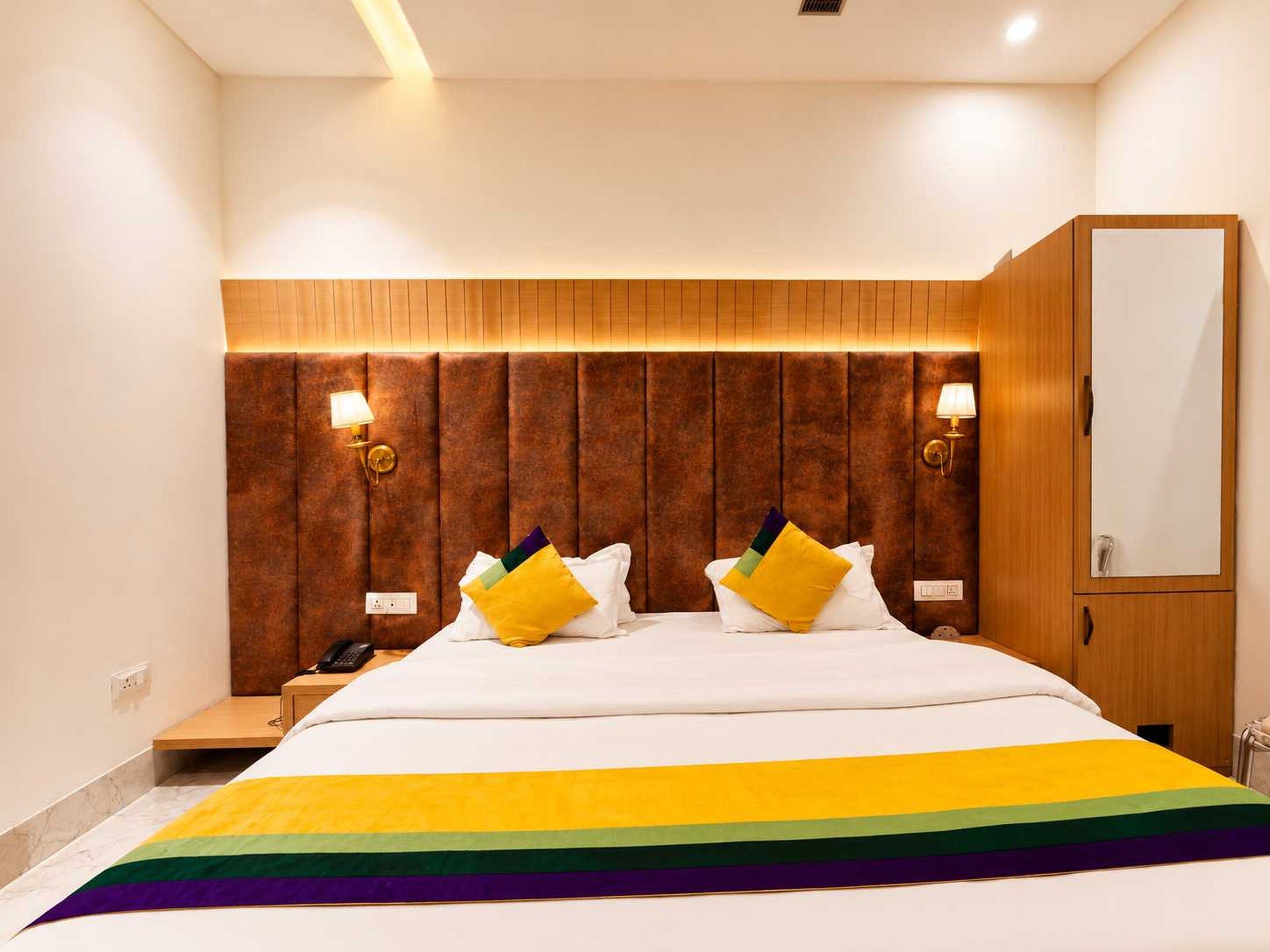 Een hotelkamer met een groot bed, een houten hoofdeinde, nachtlampjes en een spiegel.