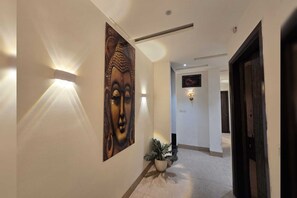 A hallway with a Buddha painting, wall sconces, and a potted plant. - Classic Sehdev Residency (Amritsar)