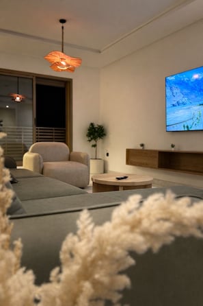 A modern living room with a sofa, a round coffee table, and a television mounted on the wall. - Modern & Luxury Apartment - (Izdihar) Marrakech (Marrakech)