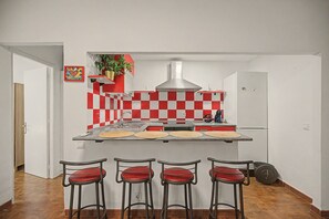 Eine Küche mit rot-weiß kariertem Fliesenspiegel, einer Edelstahl-Dunstabzugshaube und drei Barhocker mit roten Sitzflächen.
