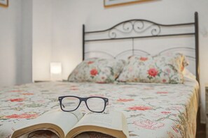 A bed with a floral bedspread, a pair of glasses on an open book, and a wall with a framed picture. - Vacation Apartment 'Ripoche 24' with Wi-Fi (Las Palmas de Gran Canaria)