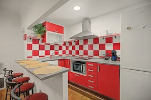 Une cuisine avec un crédence à carreaux rouges et blancs, une hotte de cuisinière en acier inoxydable, un four à micro-ondes et un réfrigérateur.