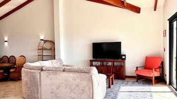 Ein Wohnzimmer mit einer Couch, einem Fernseher auf einem Holzboden, Korbmöbeln und einem roten Sessel.