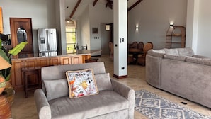 A spacious living room with a grey sofa, a patterned armchair, and a dining area with wicker furniture. - Villa Catalina 11 (Potrero)