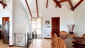 A spacious kitchen with a dining area, featuring a high ceiling with exposed beams, a modern refrigerator, and a dining table set with wicker chairs. - Villa Catalina 11 (Potrero)