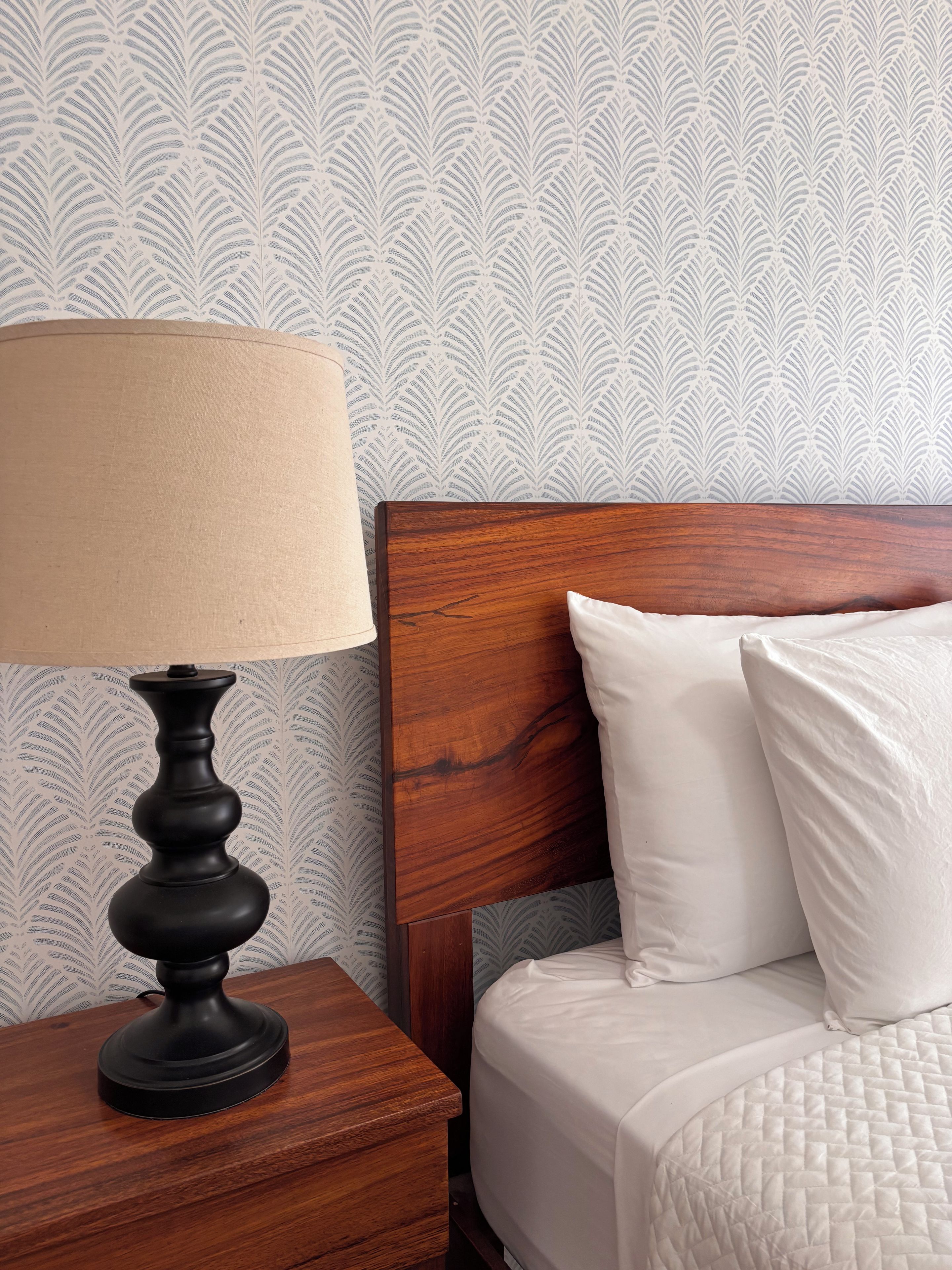 A neatly made bed with white bedding, a wooden headboard, and a nightstand with a lamp.