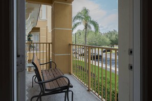 Ein Balkon mit einer Holzbank, Blick auf einen Parkplatz und eine Palme.