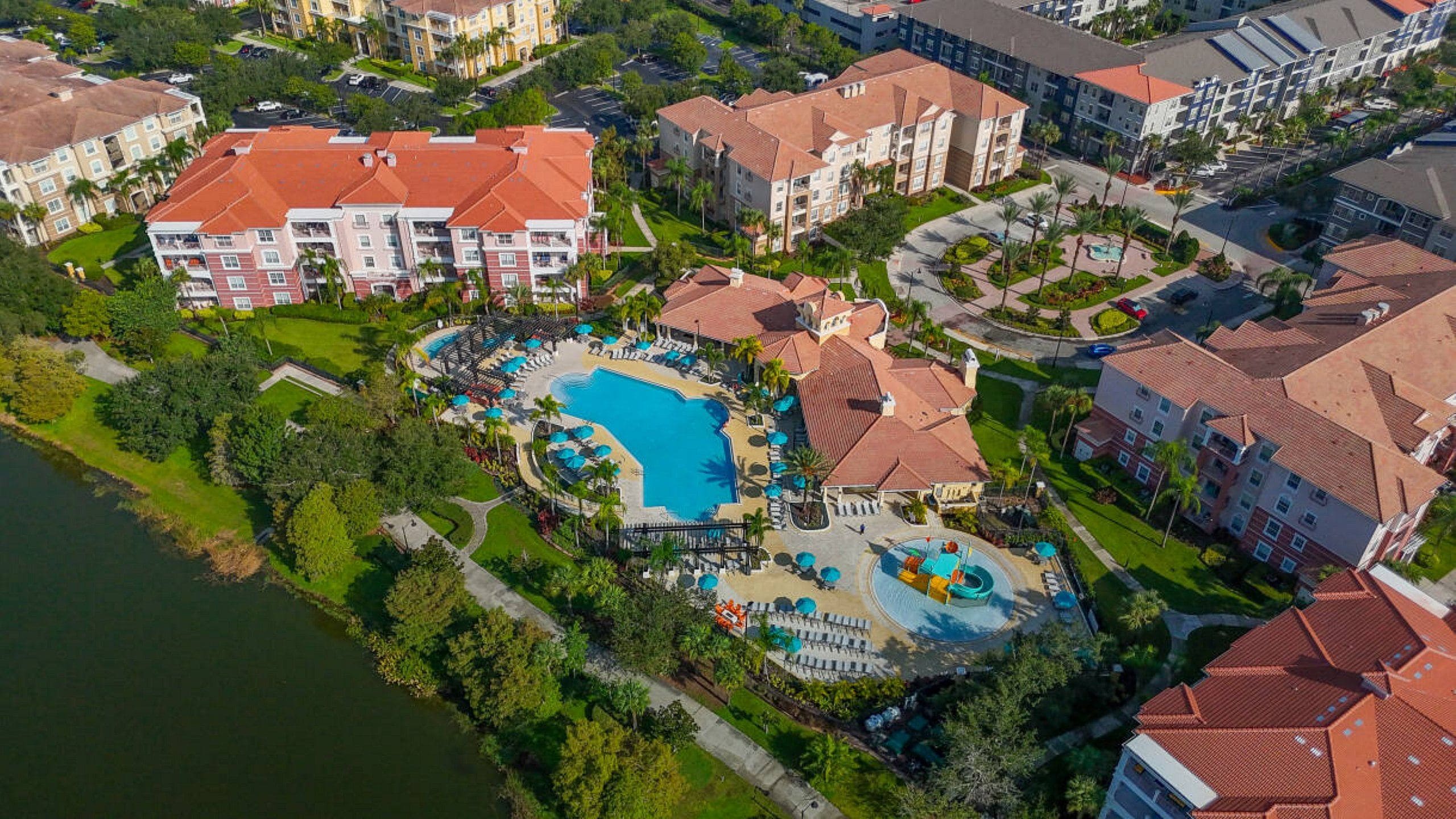 An aerial view of a resort with multiple buildings, a central swimming pool, and surrounding greenery.