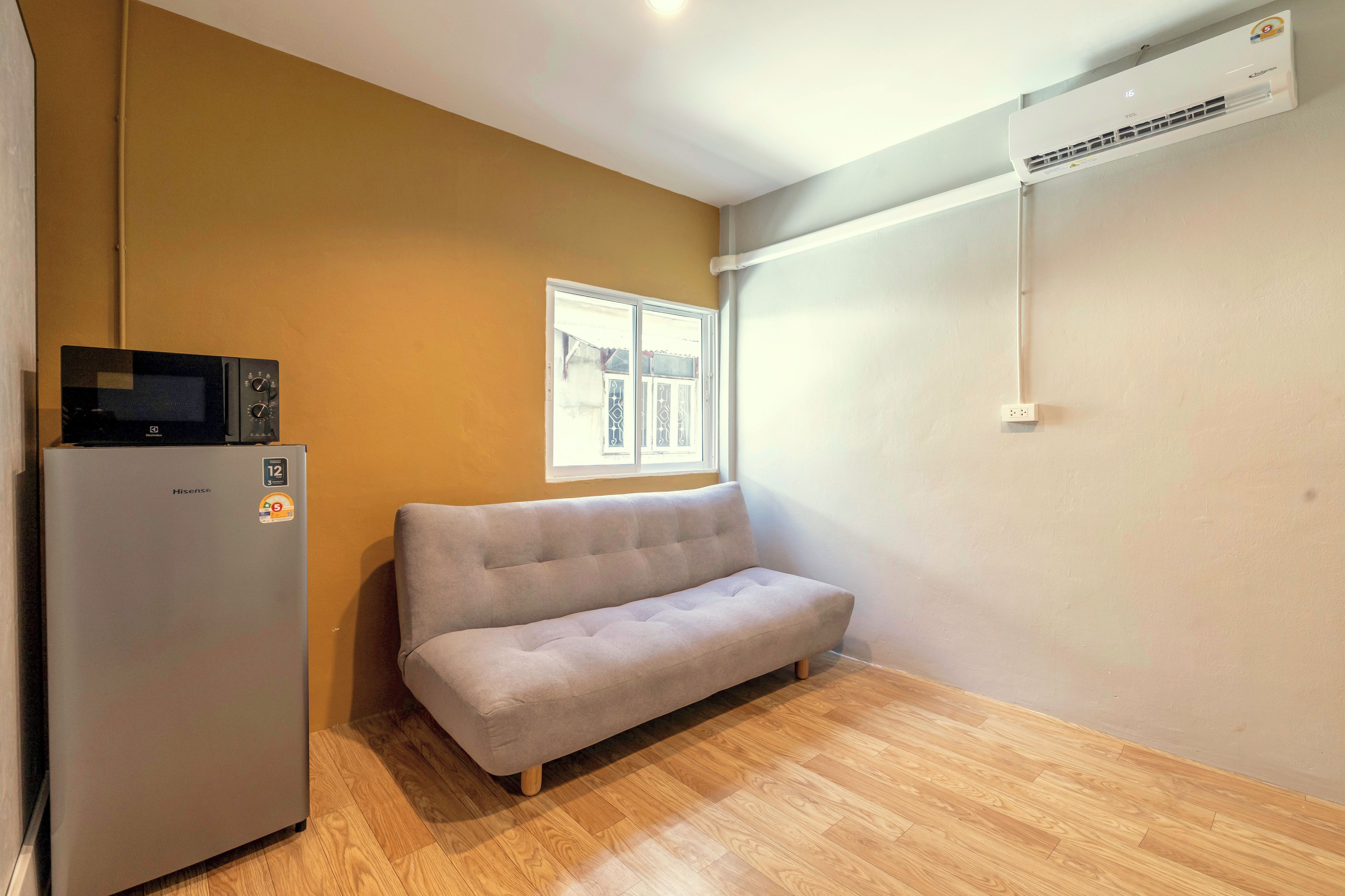 Een compacte kamer met een slaapbank, een koelkast en een airconditioning.