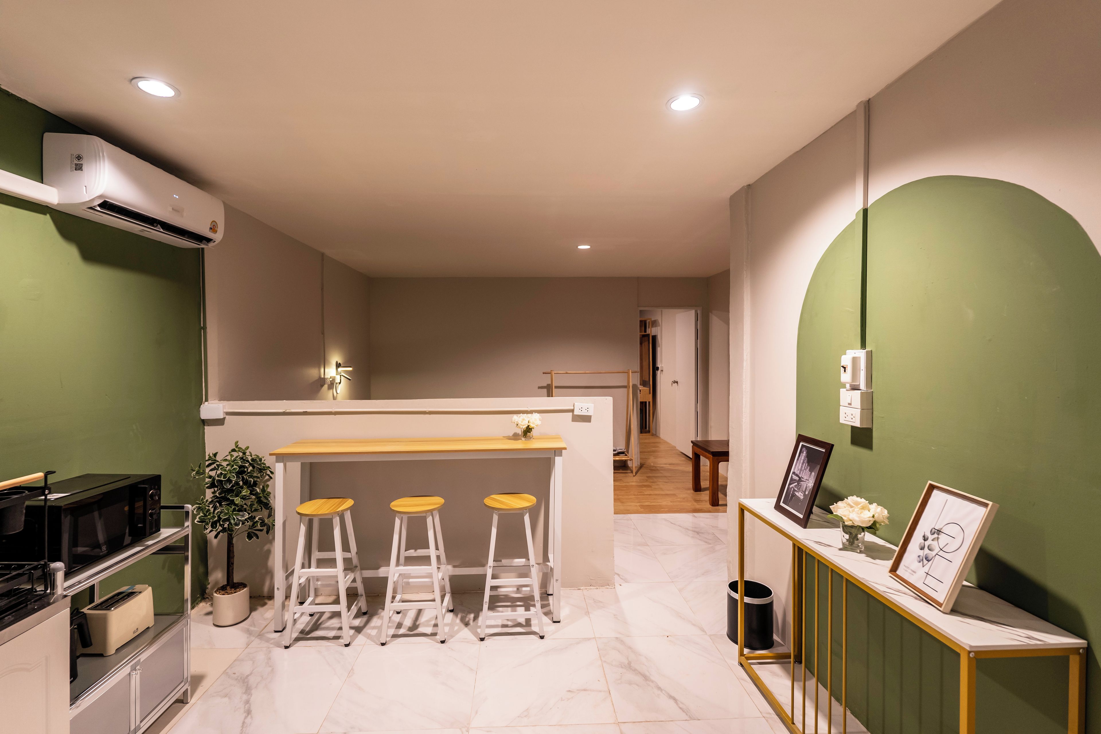 A modern kitchen with a bar area, white stools, a small dining table, and a green accent wall.