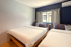 Een slaapkamer met twee bedden, een raam met gordijnen en uitzicht op de straat.