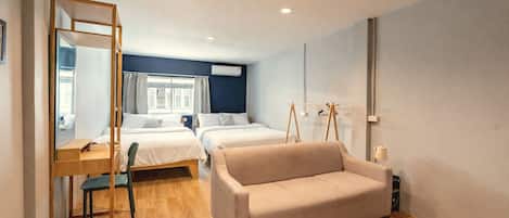A hotel room with two beds, a sofa, a desk with a chair, a mirror, and a window with curtains.