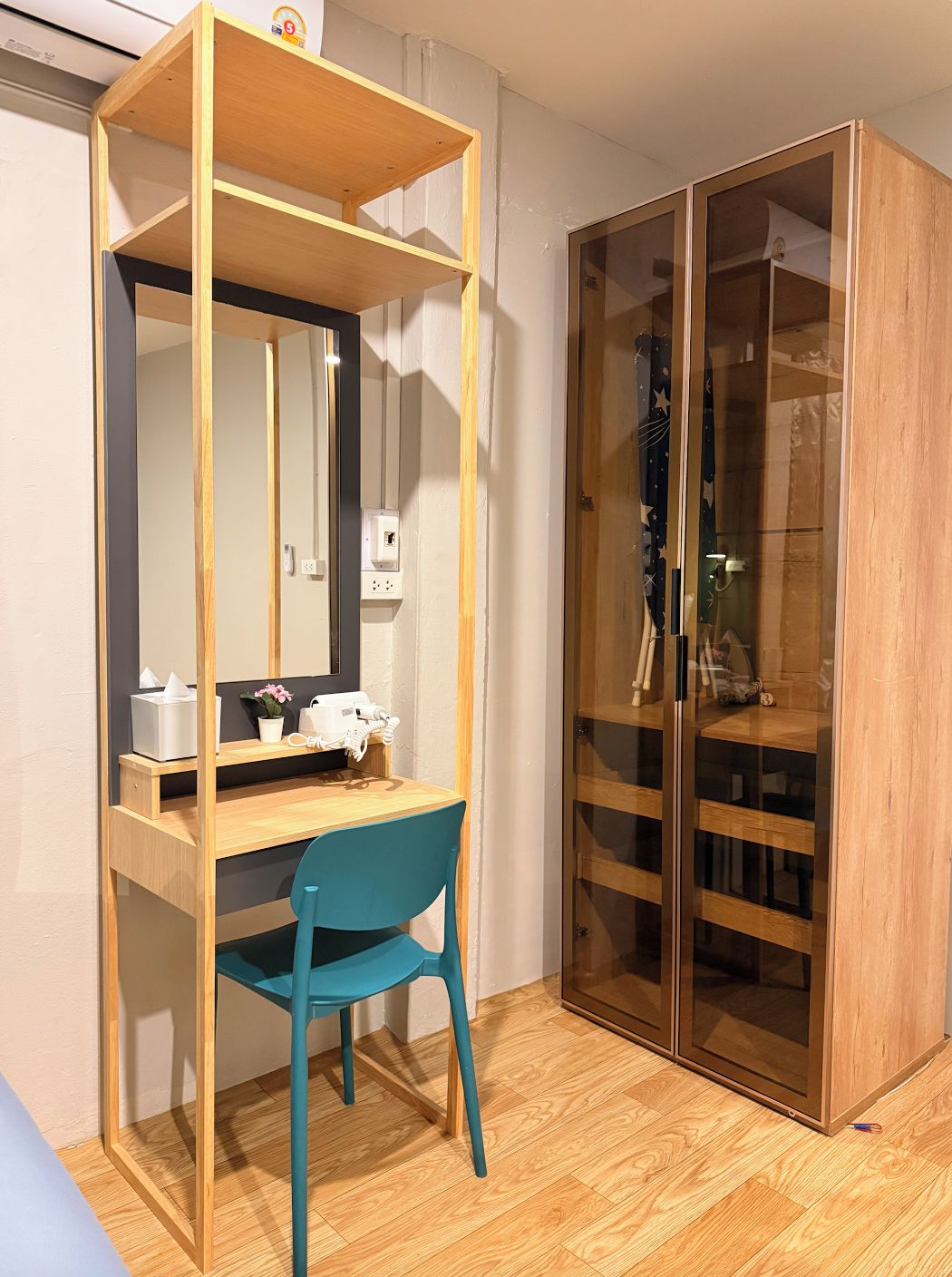 A room with a wooden desk, a blue chair, a mirror, a telephone, and a wardrobe with glass doors.