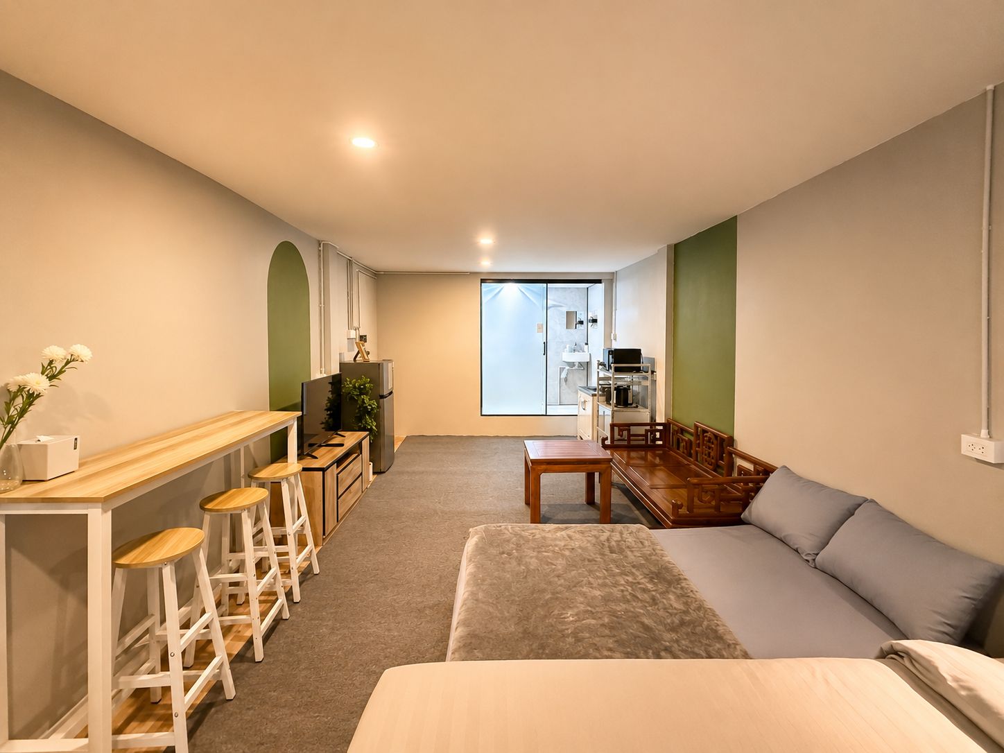Een compacte kamer met een bed, een bureau met een computer, een kleine kitchenette en uitzicht door een glazen deur.