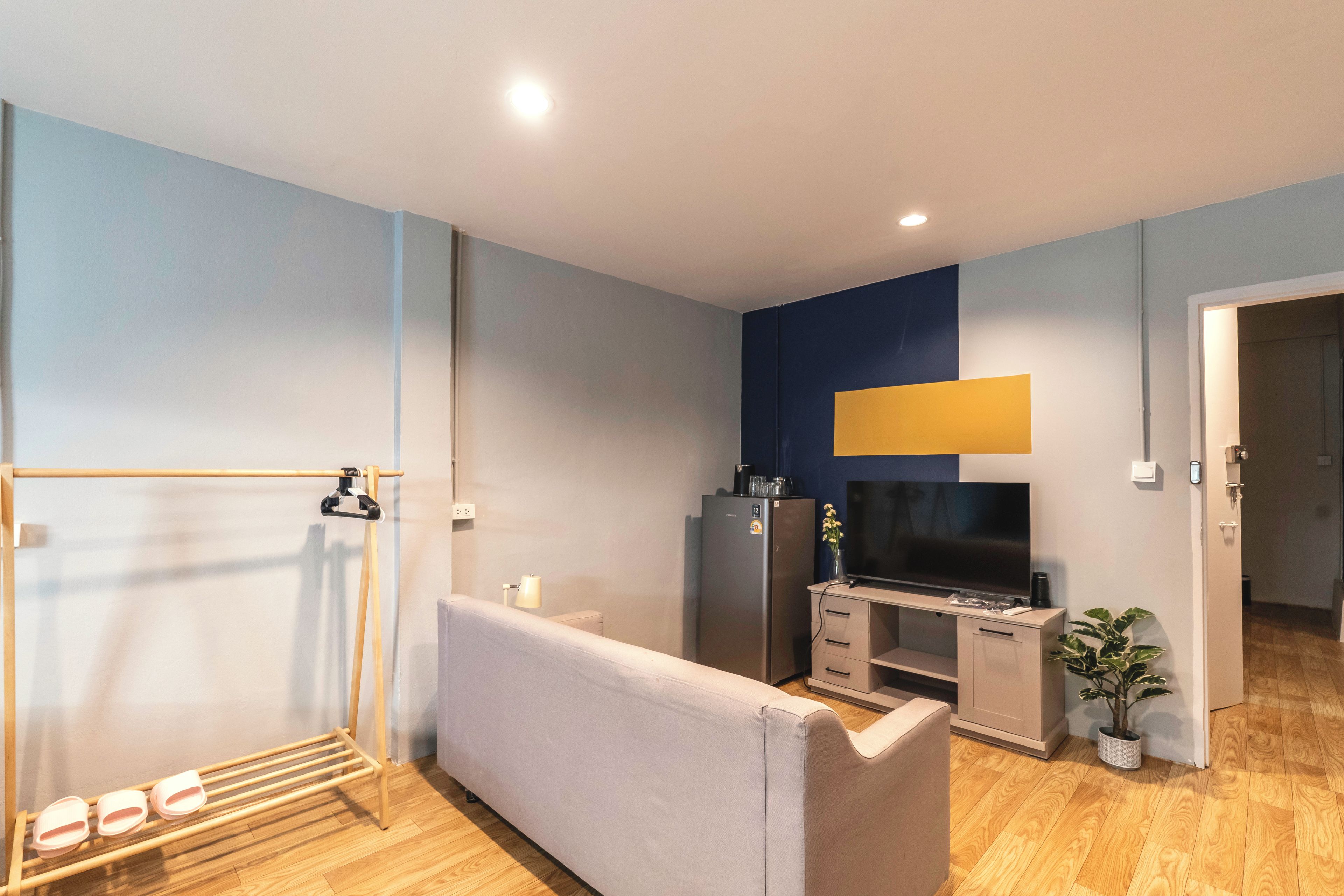 A modern living room with a sofa, a TV, a small kitchenette, and a wooden floor.
