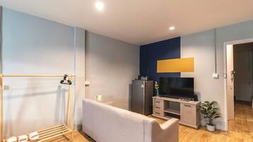 Una sala moderna con un sofá, un televisor, una kitchenette pequeña y piso de madera.