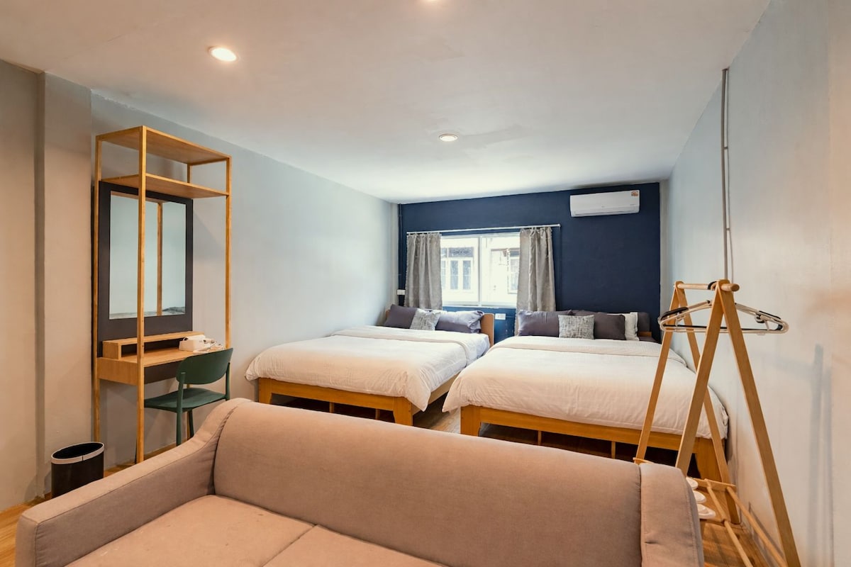Een hotelkamer met twee bedden, een bureau, een stoel, een bank en een raam met gordijnen.