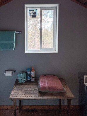 Habitació amb finestra, penjador de tovalloles, taula amb articles de tocador i una tovallola rosa.