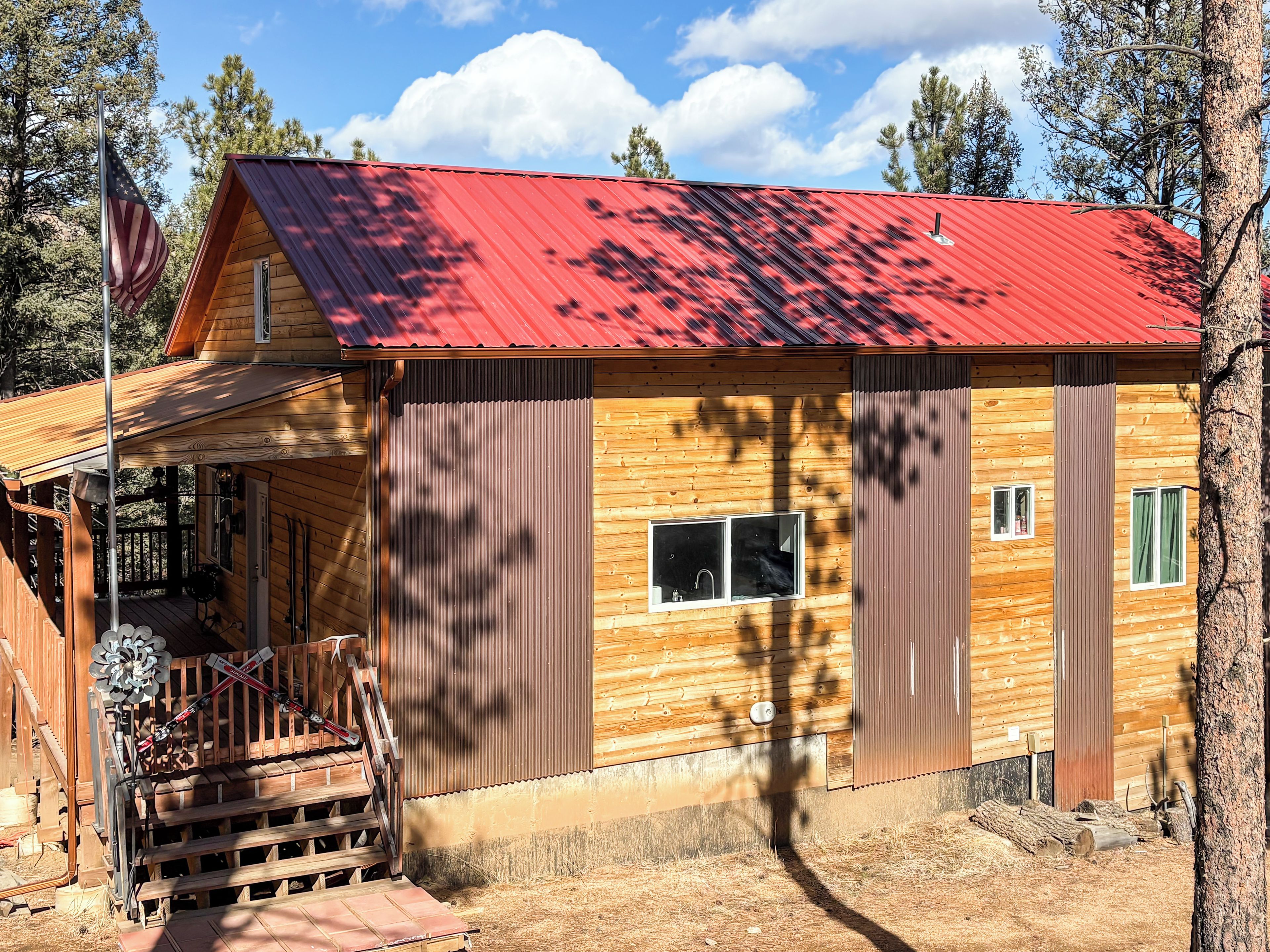 Una cabaña de madera con techo rojo, un porche y un asta de banderín.