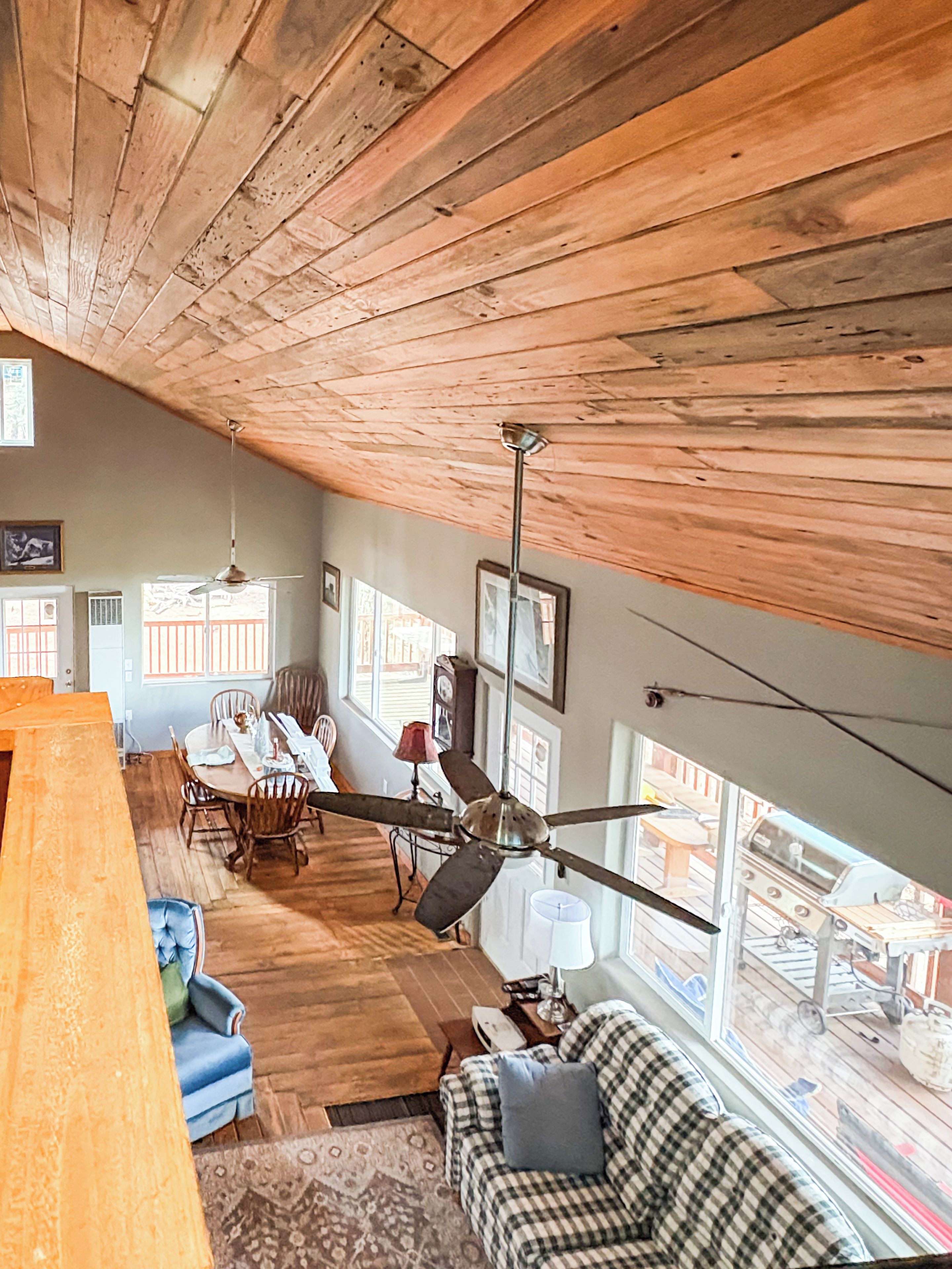 Um quarto amplo com teto alto, vigas de madeira, área de refeições com mesa e cadeiras, um sofá e um ventilador de teto.
