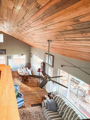 A spacious room with a high ceiling, wooden beams, a dining area with a table and chairs, a sofa, and a ceiling fan. - Ricks Mountain Retreat (Sedalia)