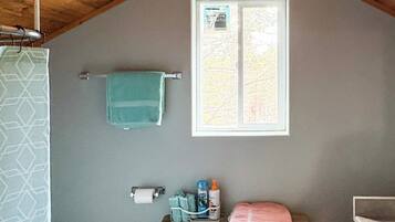 A small bathroom with a wooden ceiling, a window, a towel rack, a toilet, and a table with toiletries.