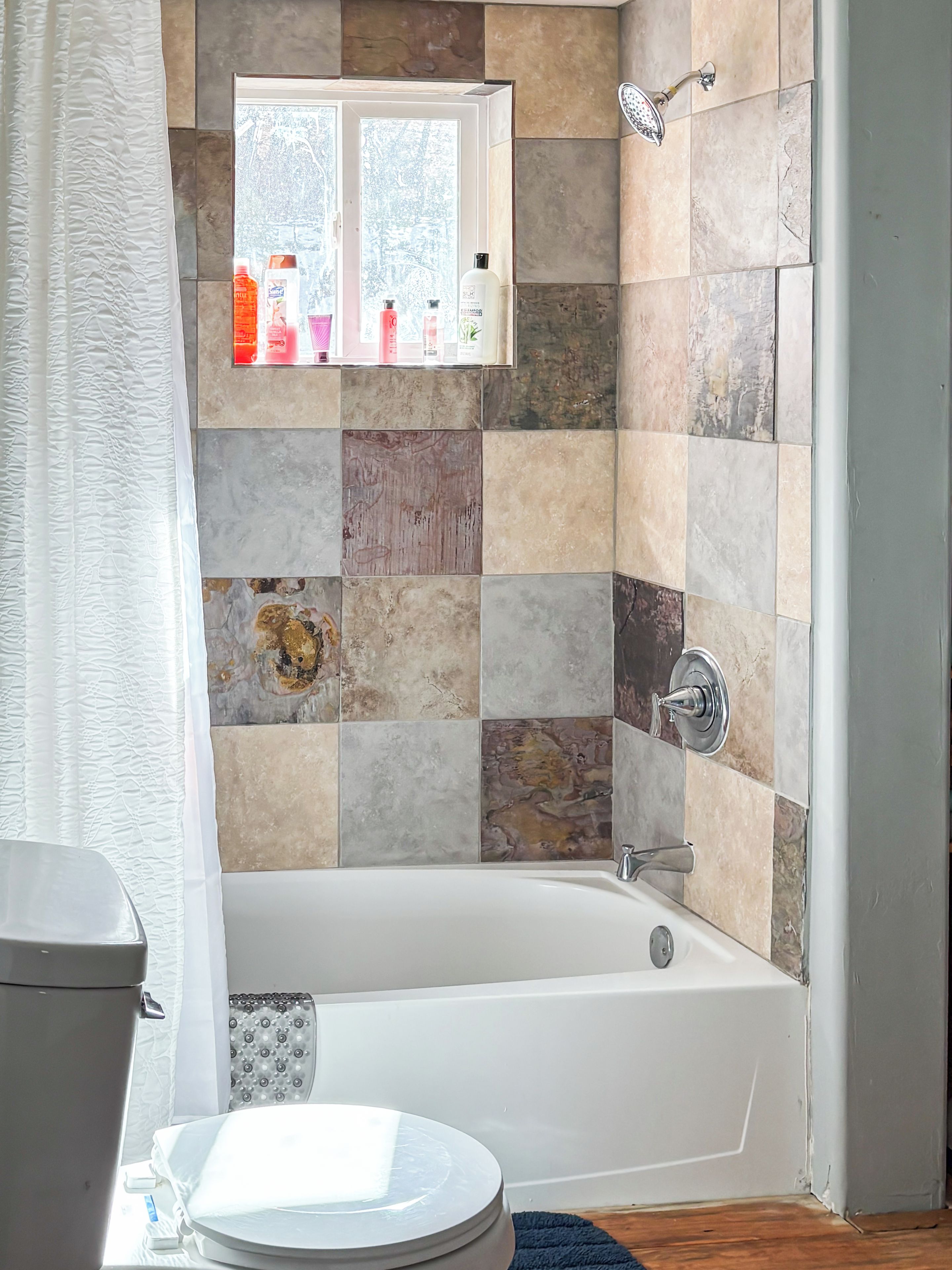 Ein Badezimmer mit Badewanne, Toilette und einem Fenster mit Toilettenartikeln.