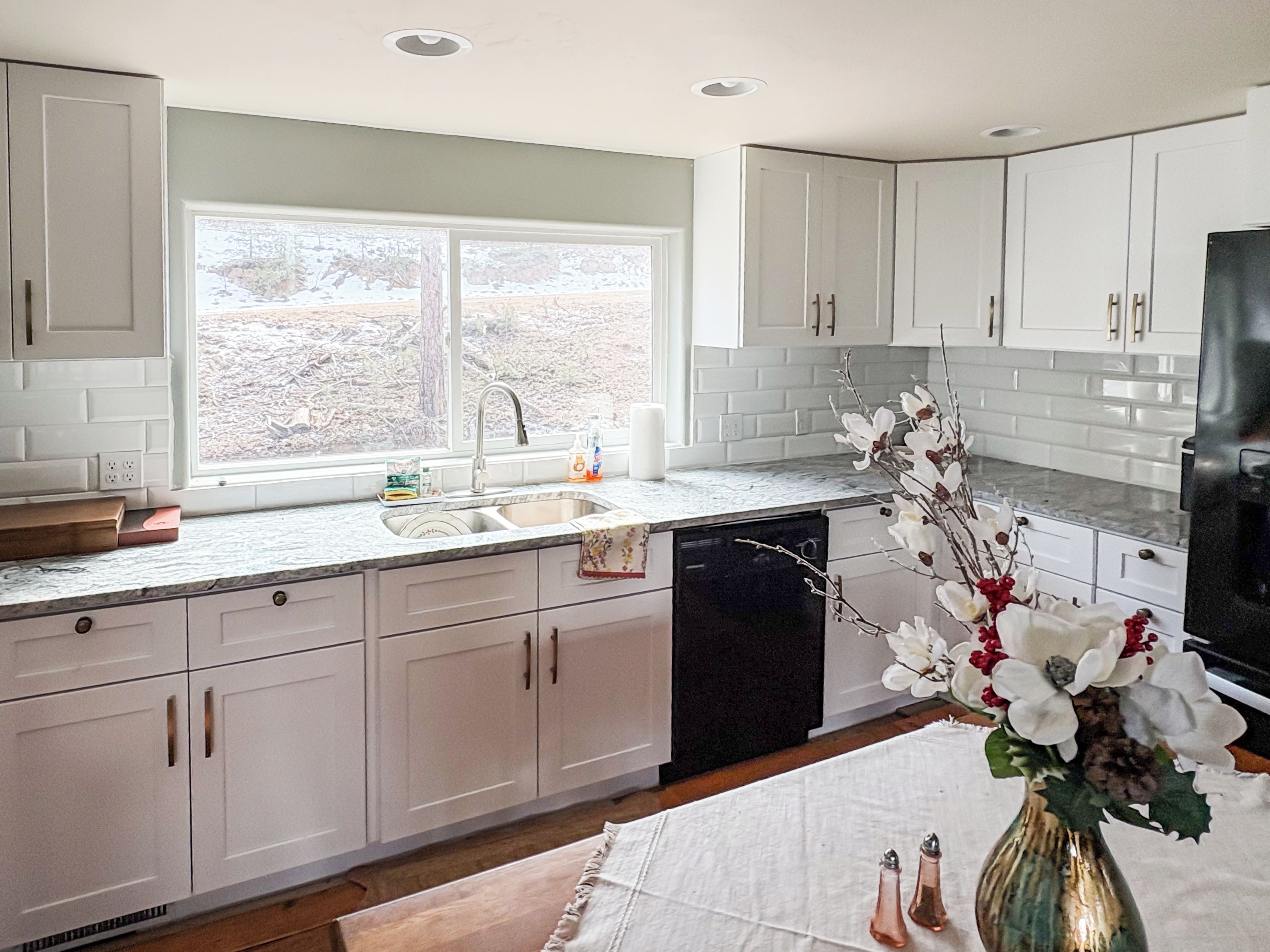 A modern kitchen with white cabinets, a built-in dishwasher, and a window providing natural light.
