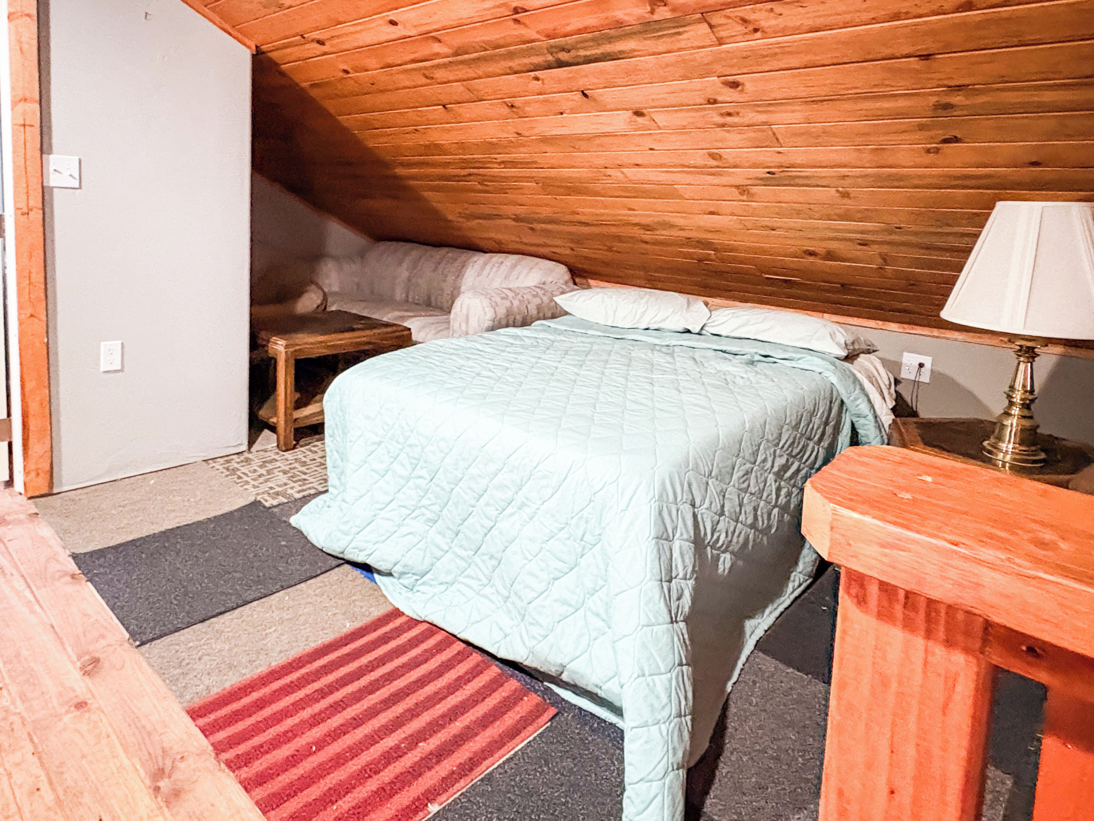 A bedroom with a bed, a nightstand, a lamp, and a wooden ceiling.