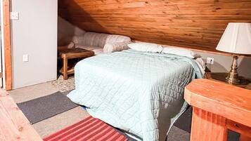 A bedroom with a bed, a nightstand, a lamp, and a wooden ceiling.