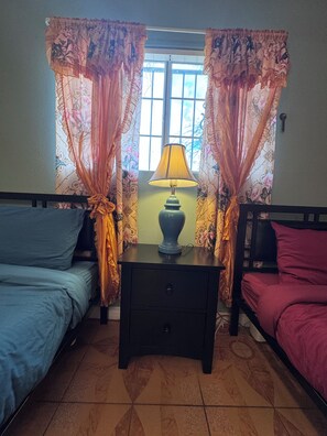 Une chambre avec deux lits, une table de chevet avec une lampe et une fenêtre avec des rideaux.