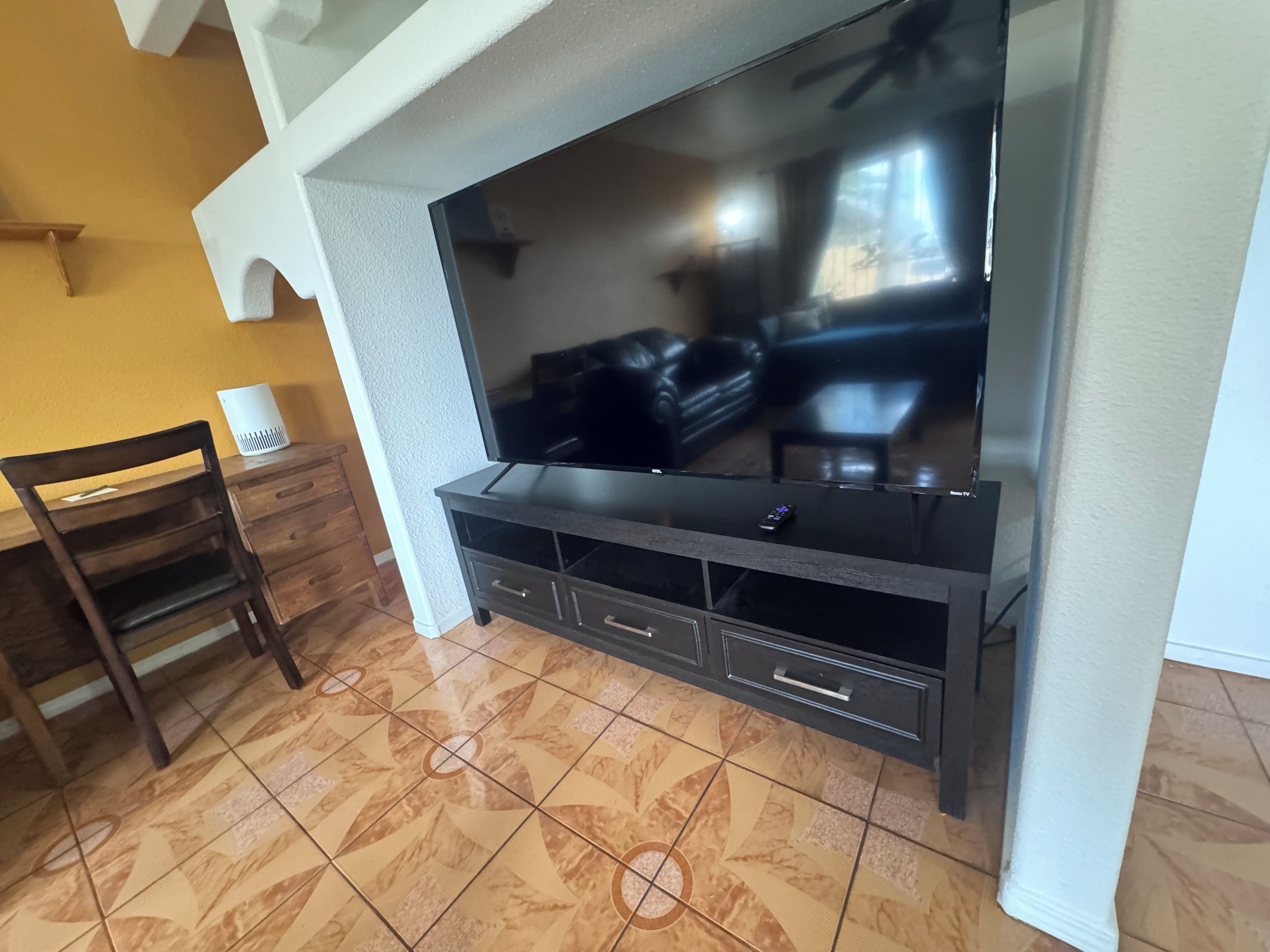 Ein Wohnzimmer mit Flachbildfernseher, dunklem Holzmöbel und gemusterten Bodenfliesen.