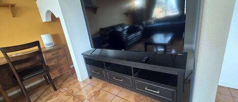 A living room with a flat-screen TV, dark wooden furniture, and patterned floor tiles.
