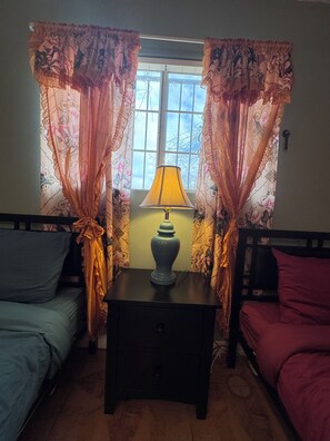 A room with a bed, a nightstand with a lamp, and curtains with floral patterns. - Next  to the strip cozy home in Vegas (North Las Vegas)