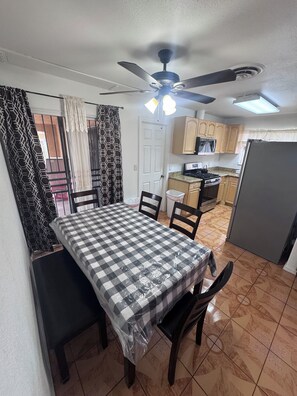 A dining area with a checkered tablecloth, chairs, a ceiling fan, and a kitchen in the background. - Next  to the strip cozy home in Vegas (North Las Vegas)