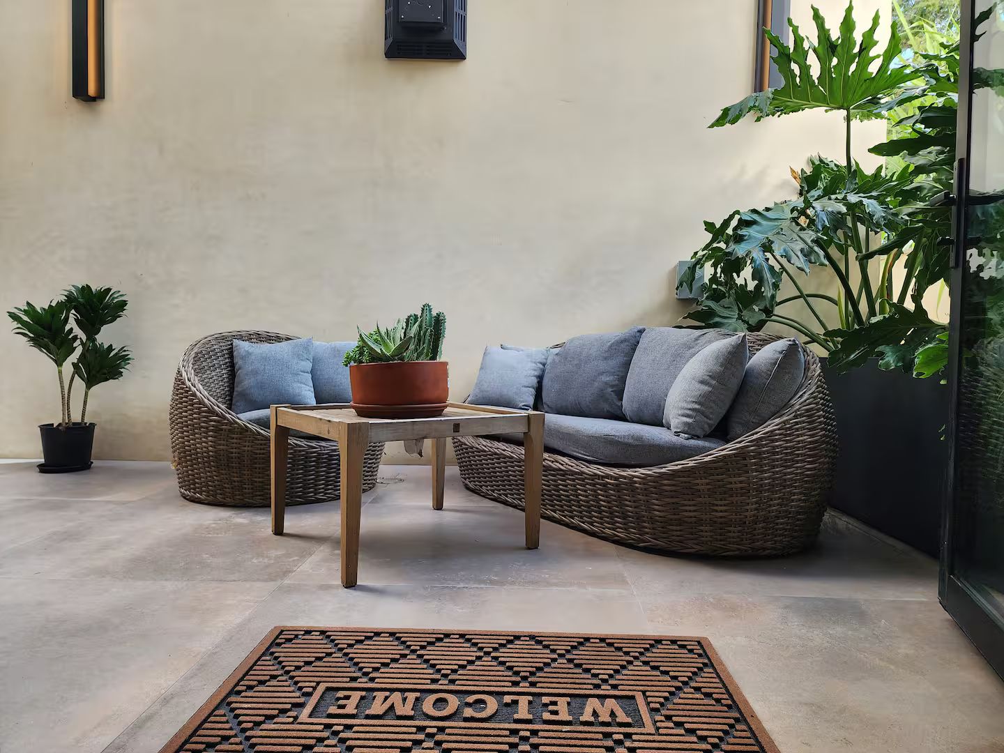 Un coin salon accueillant avec un canapé en osier, une petite table en bois et un paillasson.