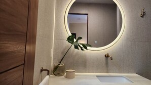 Een badkamer met een ronde spiegel, een wastafel, een handdoekhouder en een plant.