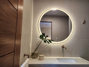 Un baño con un espejo redondo, un lavabo, un perchero para toallas y una planta.