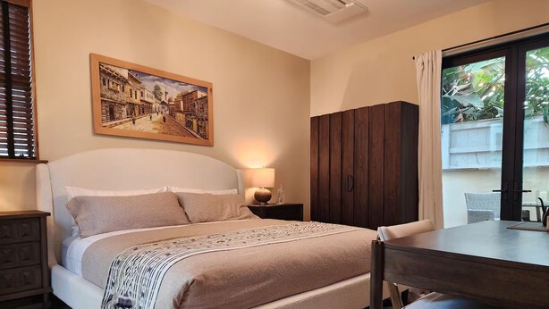 Een slaapkamer met een bed, een bureau, een stoel, een kledingkast en een schilderij aan de muur.
