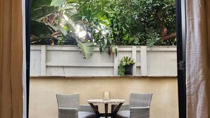 Een terras met twee rieten stoelen en een kleine ronde tafel, omgeven door een witte houten schutting en weelderige begroeiing.