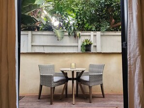 Un patio con dos sillas de mimbre y una pequeña mesa redonda, rodeado por una cerca de madera blanca y abundante follaje.