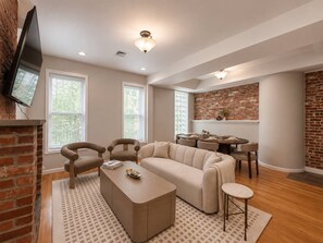 A modern living room with a sectional sofa, a coffee table, and a dining area with a brick accent wall.