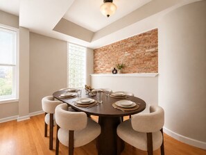 A dining area with a brick accent wall, a round table set for six, and a window with blinds.