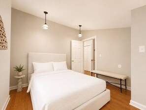 Ein Schlafzimmer mit einem großen Bett, Nachttischen, einer Bank und zwei Pendelleuchten.