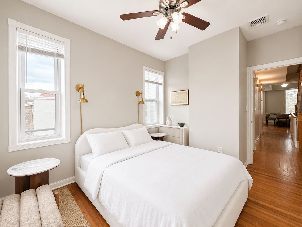 Une chambre à coucher avec un lit, des tables de chevet, un ventilateur de plafond et une vue sur le couloir.