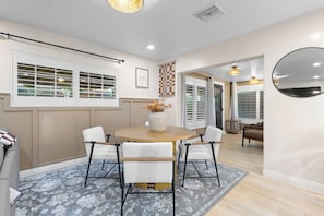 A dining area with a round table, four chairs, a vase with flowers, and a checkered wall hanging. - The Enchanted Estate , 5 Bed Rooms - 3 Bathrooms - Luxury Resort Near Disneyland (Anaheim)