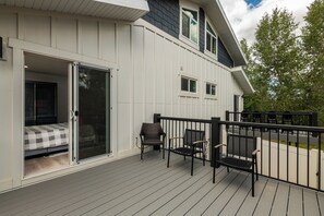 Une terrasse attenante à une maison, avec une porte-fenêtre coulissante donnant accès à une chambre, deux chaises d’extérieur et une rambarde.