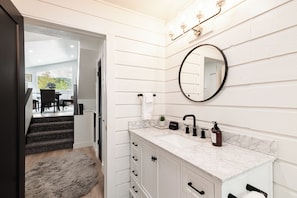 Une salle de bain avec un comptoir en marbre, un robinet noir, un miroir rond et un porte-serviettes.