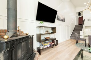 A living room with a fireplace, a flat-screen TV mounted on the wall, and a staircase leading to another level. - Park City Ski Getaway | Private Hot Tub | Fireplaces | Sleeps 10 (Park City)